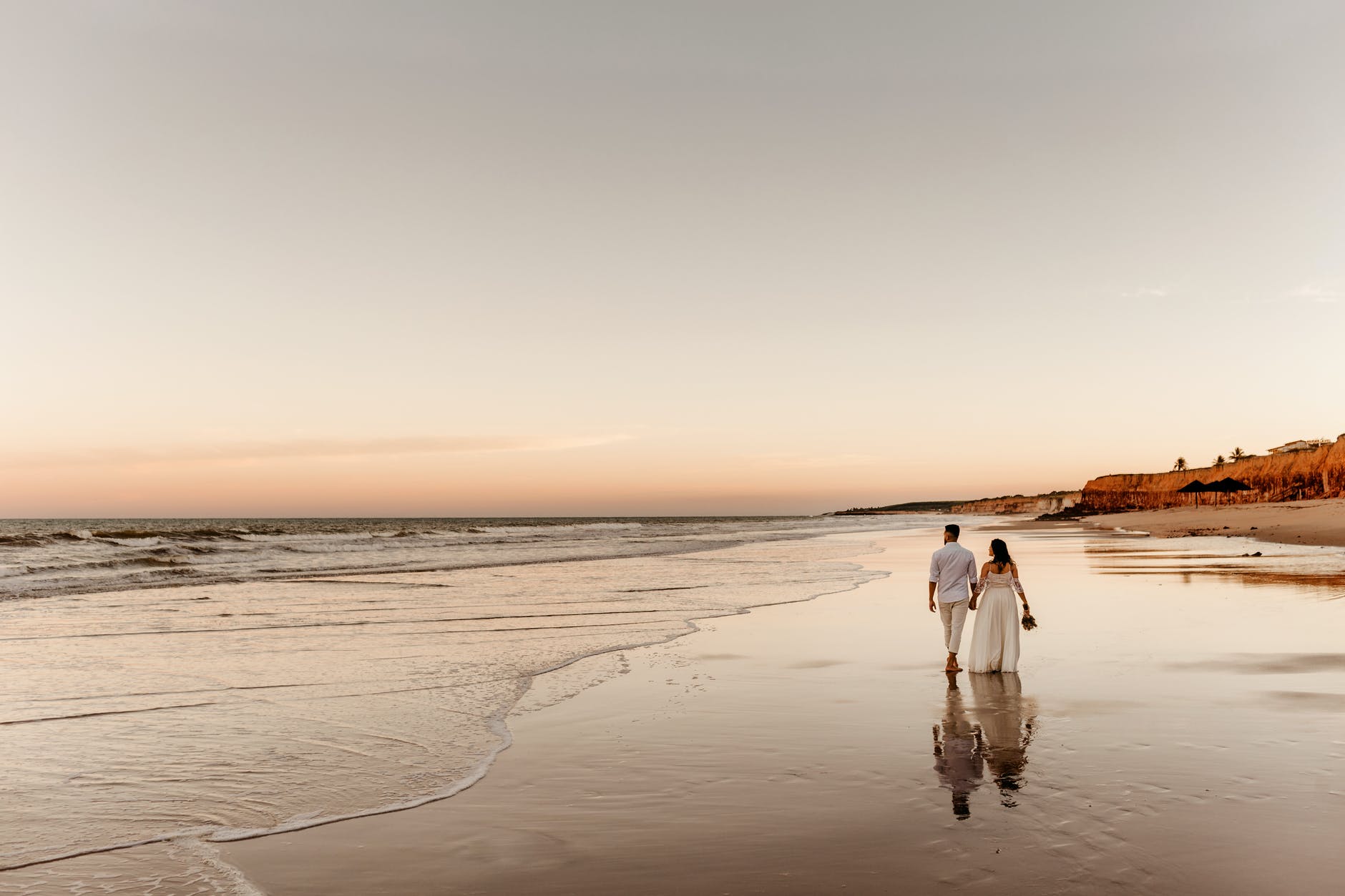 couple in wedding wear walking along seashore