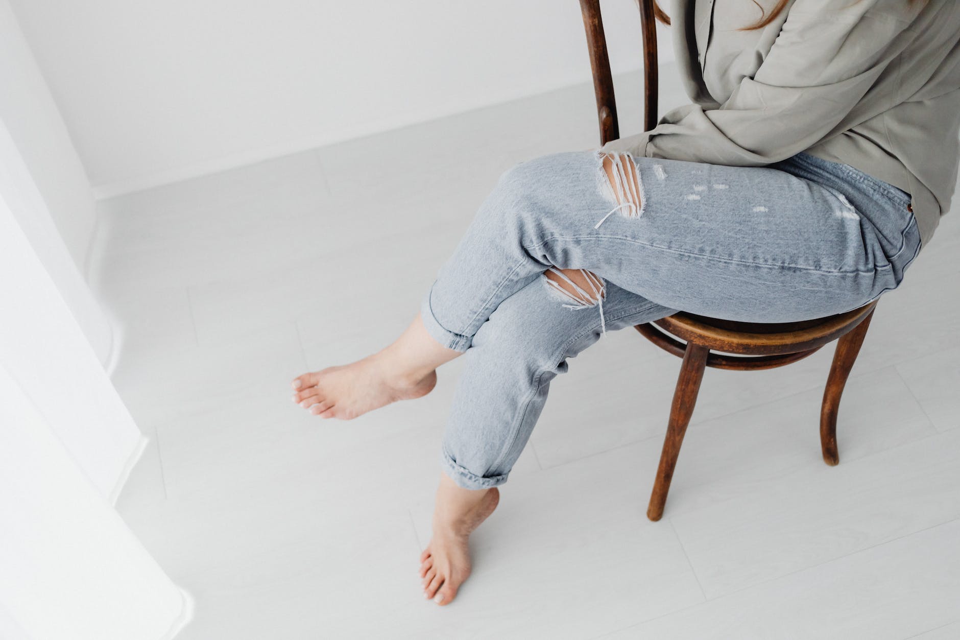 person wearing ripped jeans sitting on a wooden chair