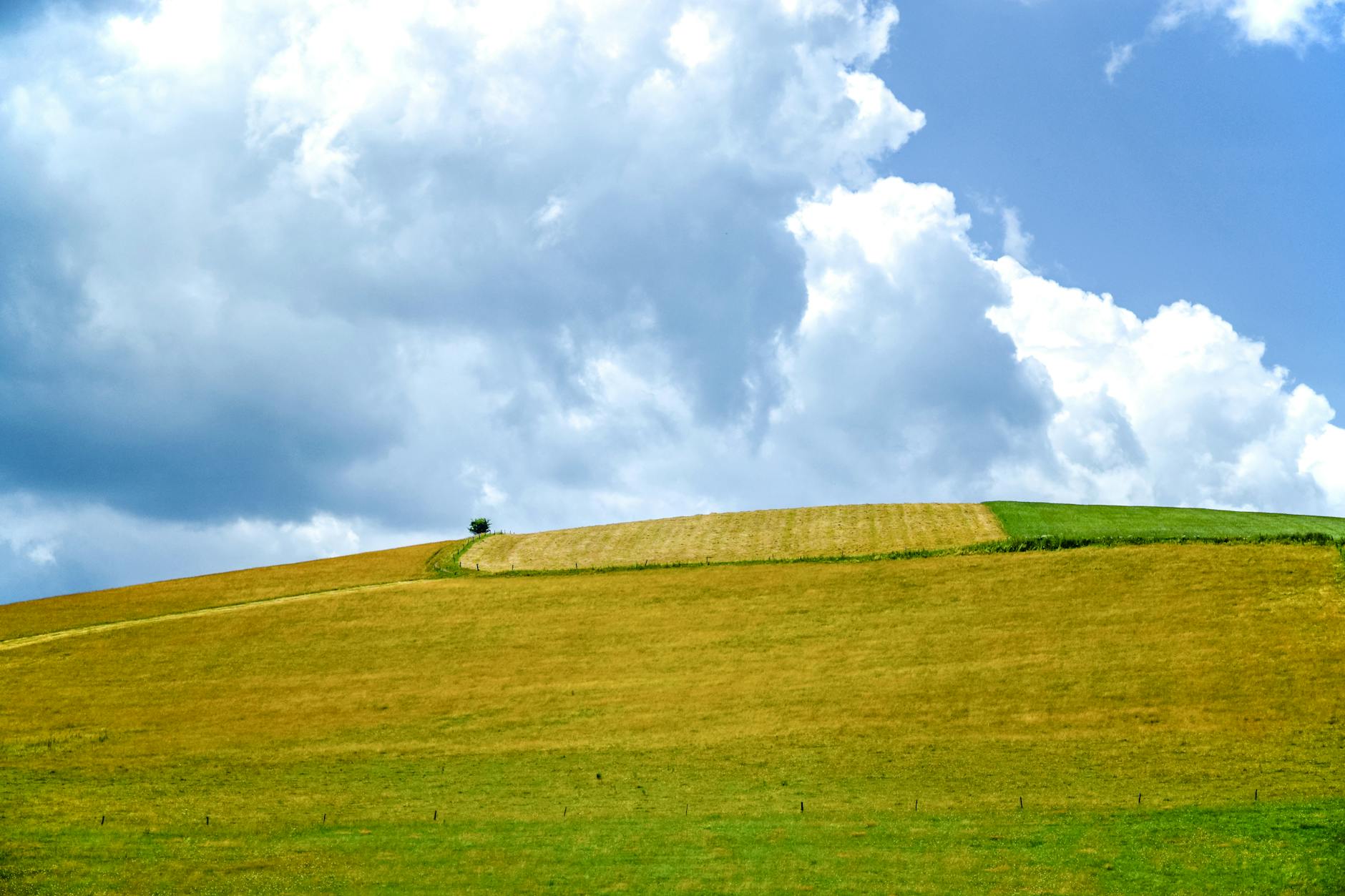 green grass covered mountain under white and blue skies
